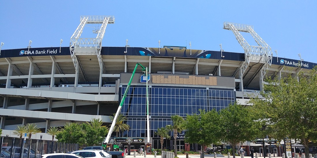 Workers lift the TIAA Bank logo into position. To the right, the stadium is prepared for the â€œTIAA Bank Fieldâ€ words.