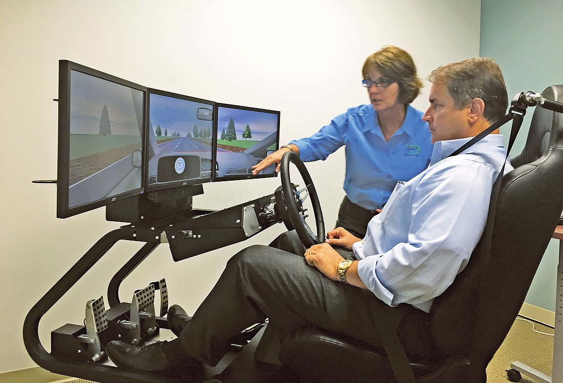 Apex Virtual Vehicle developer Trish Johnson shows Coker Law partner Matthew Posgay how to use the high-tech driver training system.