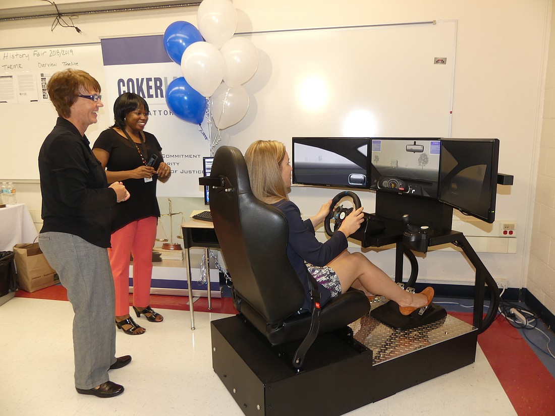 Trish Johnson, inventor of the Apex Virtual Vehicle, and Laureen Ricks, media relations supervisor for Duval County Public Schools, watch as school board member Ashley Smith Juarez tests the driverâ€™s education simulator.