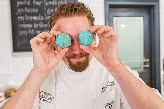 Michael Bump, executive pastry chef for Forking Amazing Restaurants, clowns around with a patron, trying on a pair of macaron eyeglasses.