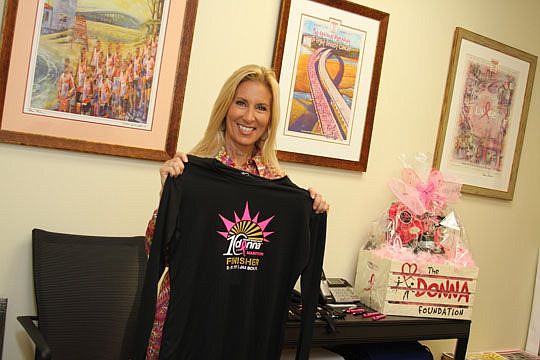 Donna Deegan holds a race T-shirt in the meeting room at The Donna Foundation headquarters. The room is decorated with marathon commemorative posters from the marathon's past years.