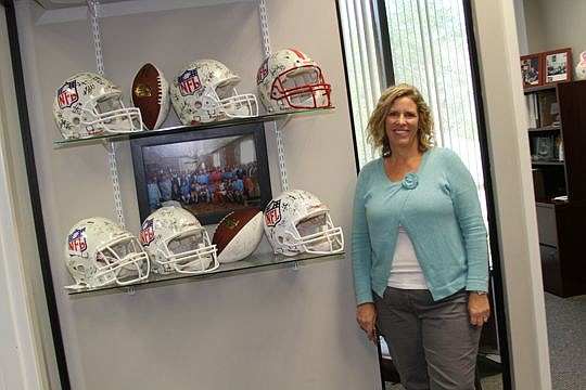 Keli Coughlin, executive director of the Tom Coughlin Jay Fund, by a series of autographed football helmets in the reception area at the nonprofit's office in Ponte Vedra Beach.