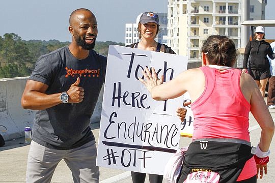 Stephan Hartley of Orangetheory Fitness holds up an endurance sign to encourage runners as Jessica Tharpe looks on.