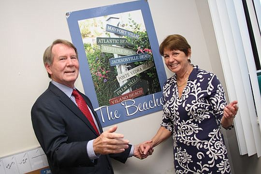 Neil and Kathie McGuinness at their Keller Williams Southside office, in front of a mock-up of the cover of a book written by Neil, who writes history books as a hobby.
