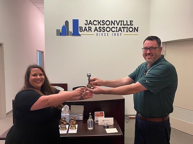 Attorney Kathryn Stanfill accepts, properly socially distanced, the first-place trophy for the Jacksonville Bar Association miniature golf tournament at the Oct. 16 barbecue from JBA Executive Dorector Craig Shoup.