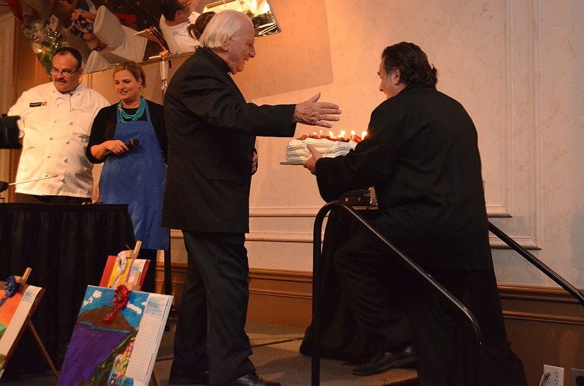 Phil Mancini brings out the surprise birthday cake for Fr. Fausto Stampiglia.