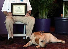 Marty rests while his owner, Ken Miles, sits with his diploma during the graduation ceremony.