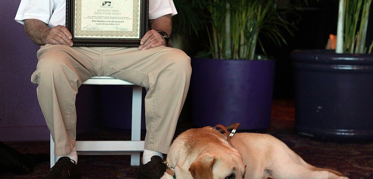Marty rests while his owner, Ken Miles, sits with his diploma during the graduation ceremony.