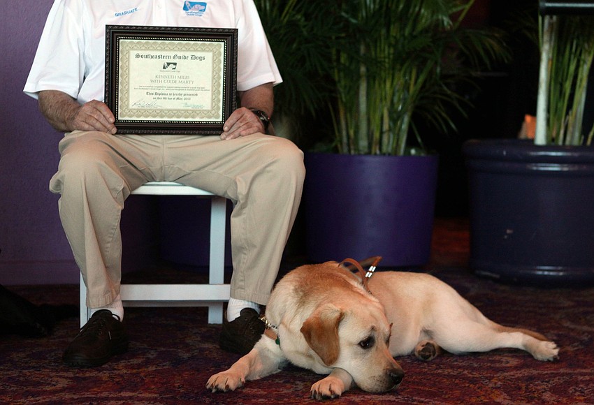 Marty rests while his owner, Ken Miles, sits with his diploma during the graduation ceremony.
