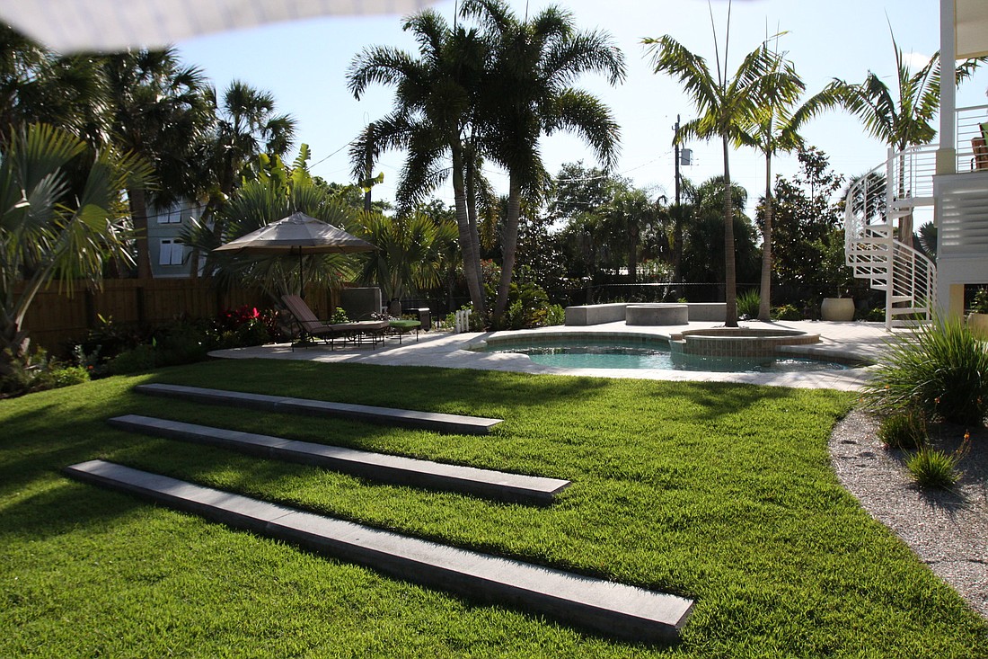 The backyard features a large grassy area with concrete steps leading to the patio, which features a refinished pool and a custom-made fire pit.