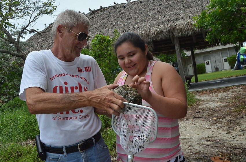 Bill Johnson holds out a 40- year-old snail for Chrissy Lopez to touch. Chrissy found the snail in the bay.