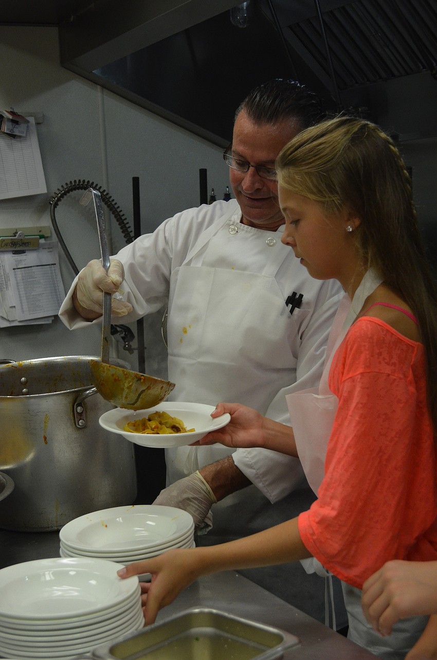Chef Ken Smith spoons Bolognese sauce into the bowl for camper Samantha Reisky.