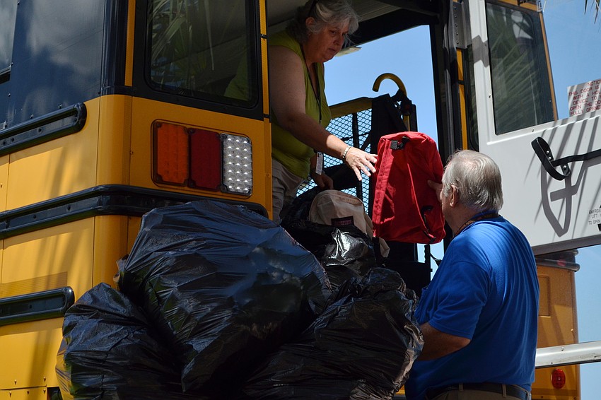 Bus drivers Loice Carpenter and Craig Taylor load bags full of backpacks into a school bus.