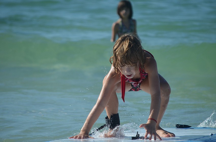 Isabelle Zamora, 6, gets ready to stand on the board as she coasts into shore.