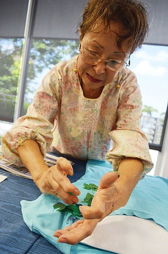Aiko Anderson demonstrates calligraphy painting on T-shirts. She imprints a leaf onto the shirt to make a floral design.