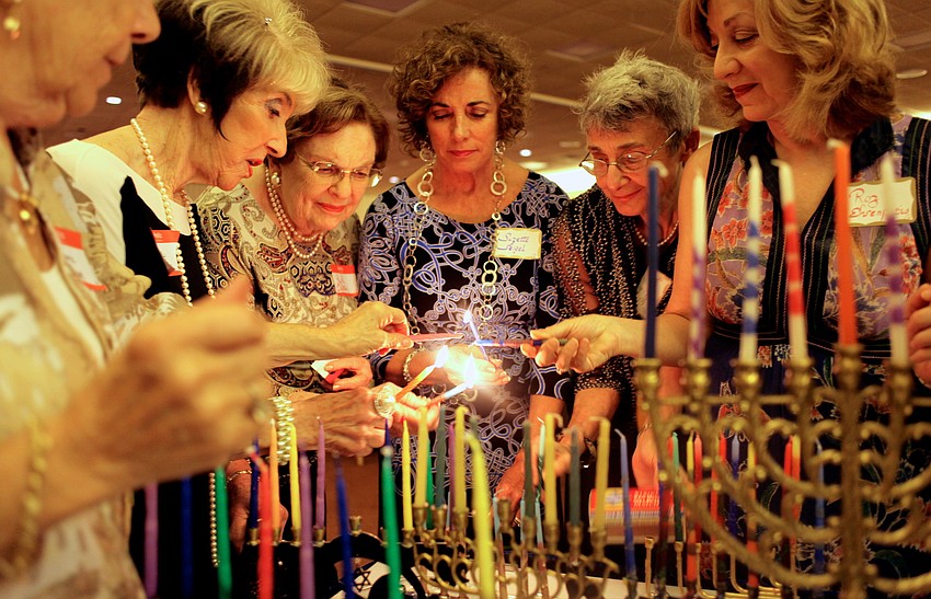 Representatives from each table gather to light 14 unique menorahs.