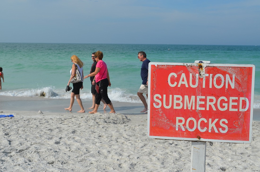 Beachgoers walk past exposed rocks on eroded sections of Lido Beach Monday, April 1.