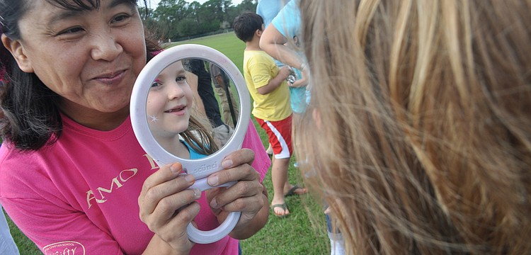 Face painting artist Akiko Campbell shows Abigail Pfeiffer, 6, the rainbow on her face.