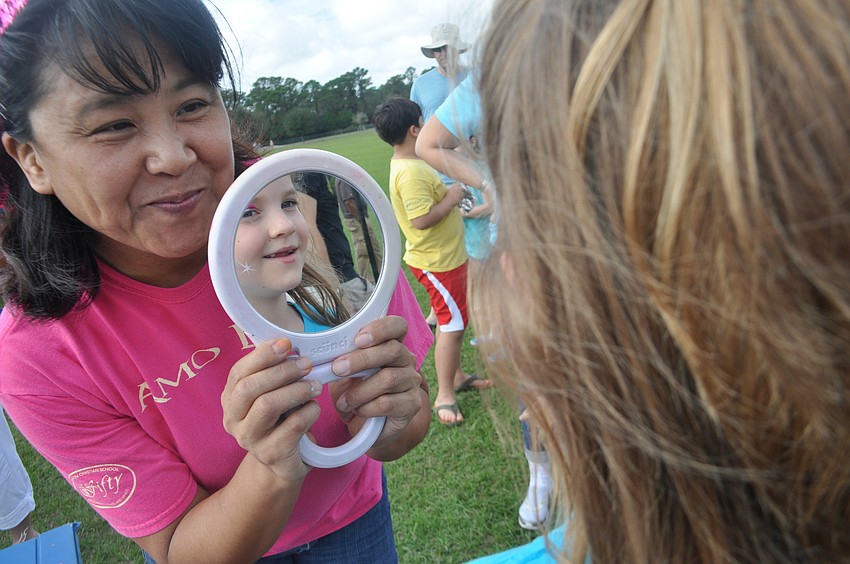 Face painting artist Akiko Campbell shows Abigail Pfeiffer, 6, the rainbow on her face.