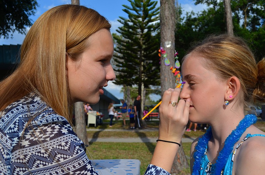 Michelle McFall paints multi-colored polka dots on Lizzy Dawsonâ€™s face.