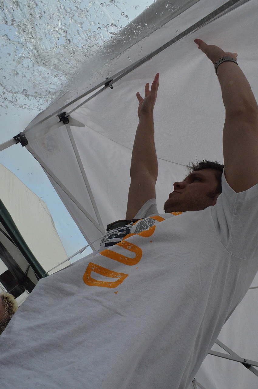 Volunteer Michael Zitani pushes water off the tent as the rain pours down on the blood drive.