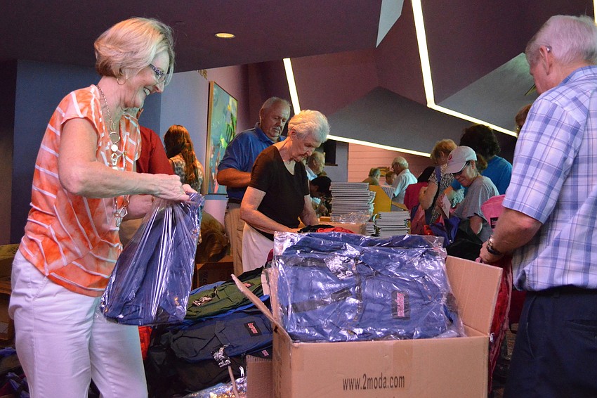 Volunteers on one side of the table prepare the supplies for the backpacks.