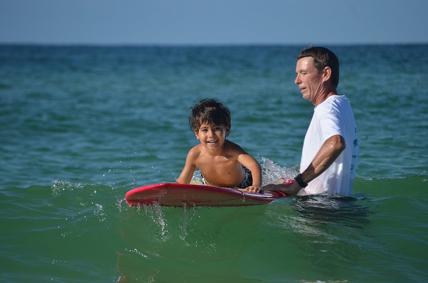 Surfers and in water volunteers help Benjamin Lalo, 5, catch a wave.