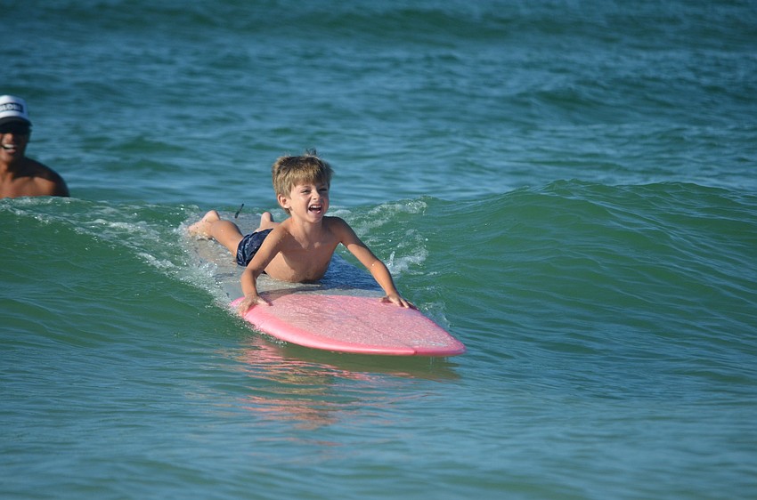 Surfer Chris Marquez helps Kolbe Huffman, 7, catch a wave. Kolbe excitedly hopped on the surfboard. This was his fourth time at the event.