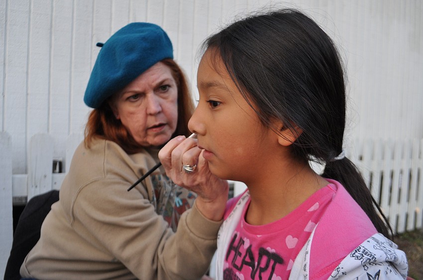 Art teacher Pat Knowlton adds glitter to the butterfly on the face of Desiree Delgado, 9.