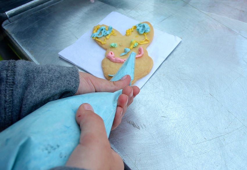 Children decorate bunny and egg-shaped cookies at the Easter celebration.