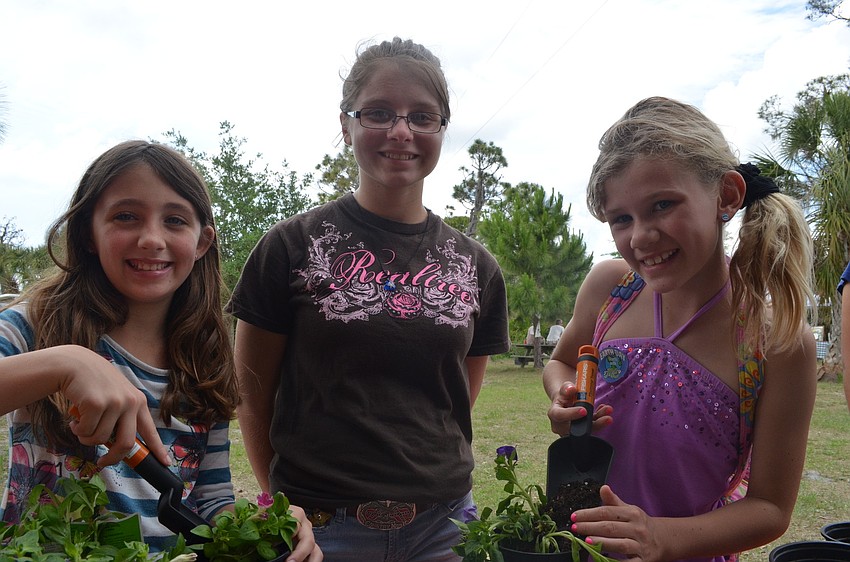 Hailey Pearc, Brandi Carroll and Mary Kate Day plant flowers in pots at the Home Depot stand.