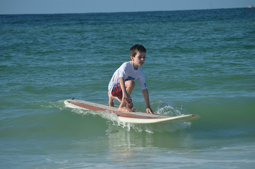 Harrison Troyan, 6, begins to get the hang of surfing. He stands on the board as he coasts into shore.