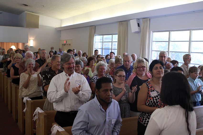 The families of the scholarship recipients and members of the church stand and applaud the 18 students.
