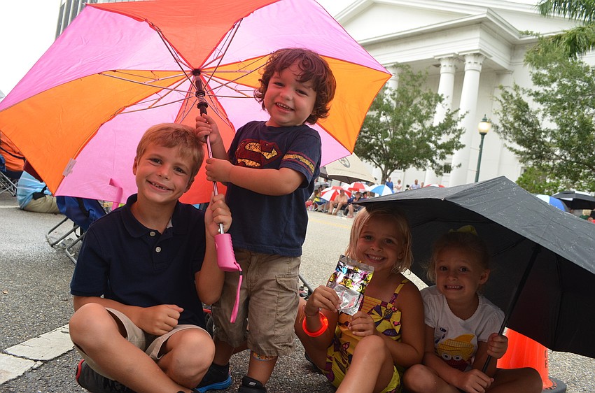 Landon Marsters, 6, Dylan Carrillo, 2, Tegan Hoffman, 5, and Madelyn Marsters, 4, hide underneath umbrellas as the rain begins at the start of the parade.