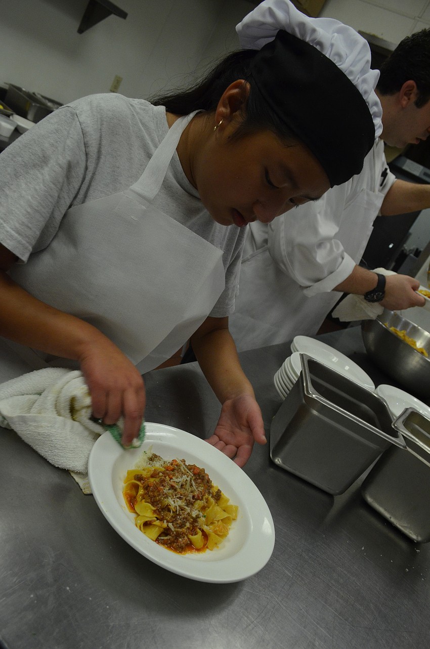 Jennifer Woodford, 14, wipes off any excess Bolognese sauce from the side of the plates. Campers learned that the presentation of a dish is also very important.