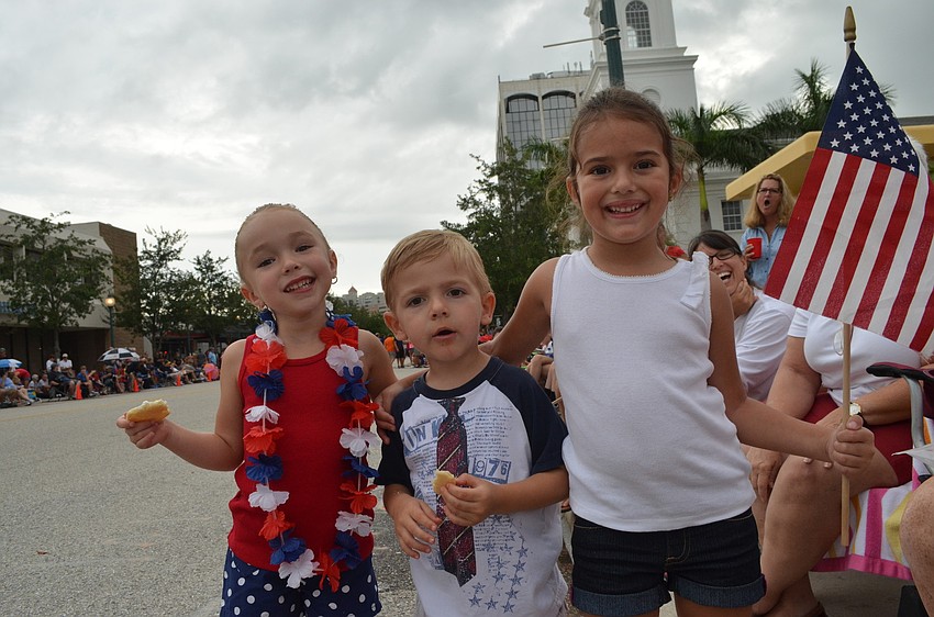 Lauren Sabbattini, 5, Jack Wilson, 3, and Addison Williams, 4, wave their flags and eat cookies on Main Street during the parade.