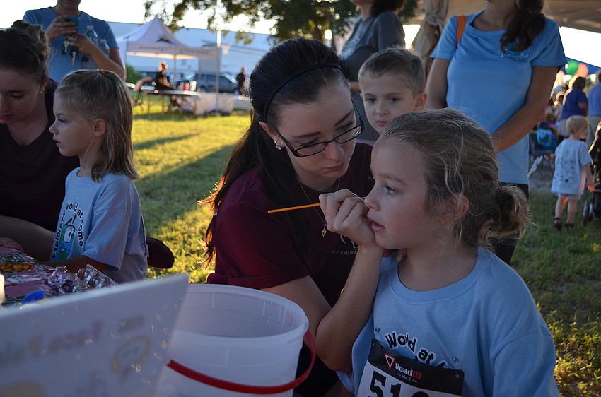Paige Vena paints a bat on Riley Lococoâ€™s face at the face painting station.
