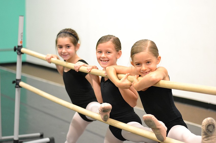 Lila Tack, Emma Zamikoff and Iris Axelius smile during leg stretches.