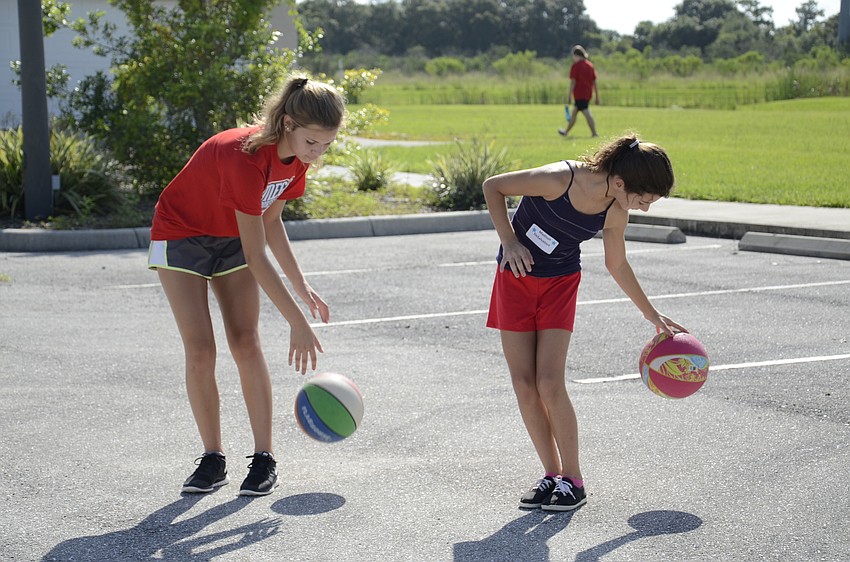 Camp volunteer Ramsi Forst and Madison DeSalvatore practice dribbling around their legs.