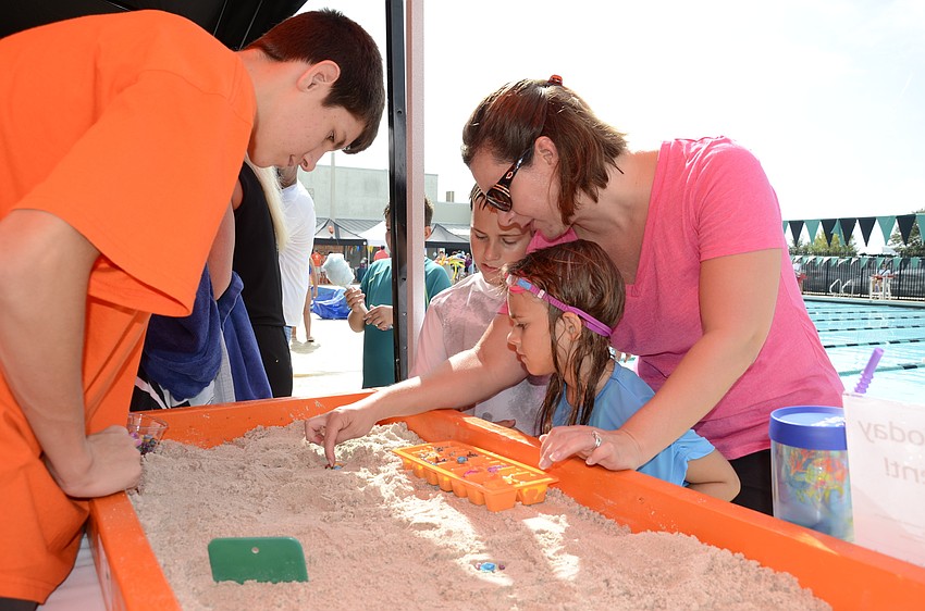 Easton Evans, 15, helps Nicole, Liz, 6, and Nate Bentze, 9, arrange a sand creation at the Island Time Treasures booth.