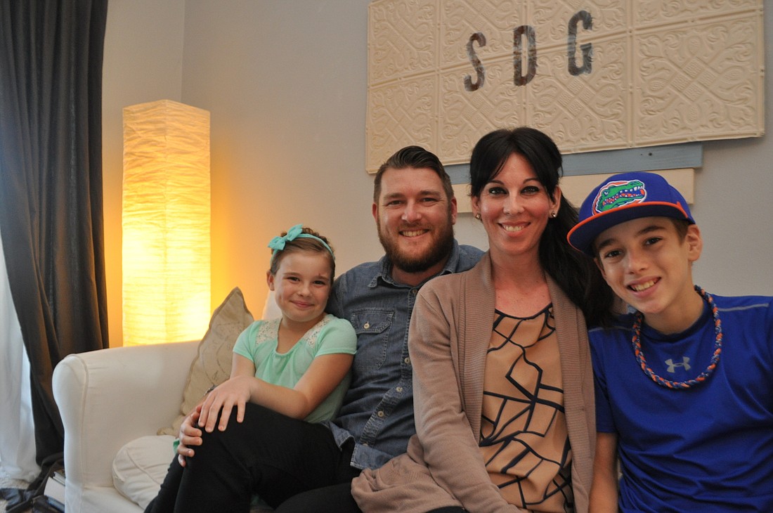 Pam Eubanks London, Pilgrim, Jenny and Aiden Benham sit beneath a sign that hangs in the living room of their Creekwood home that says â€œSDG.â€ The letters stand for â€œsoli Deo gloria,â€ or â€œAll glory to God.â€ Bach wrote the reference at the bottom of all his