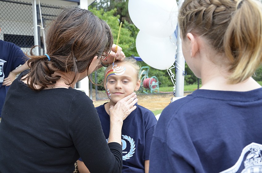 Patty Erwin with Pixie Painting finishes the rainbow design on Mia Proctor's face, while her younger sister Olivia watches.
