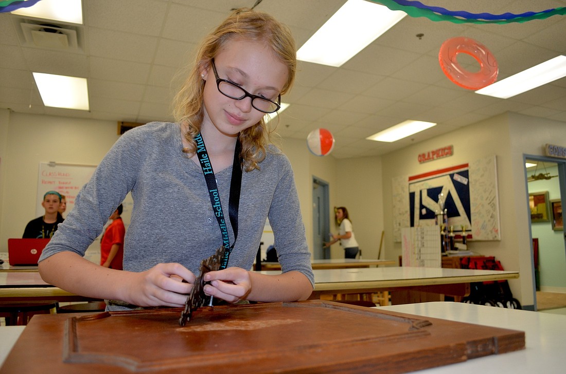 Seventh-grader Katie Love unhinges a knob from an old cabinet door.