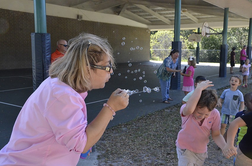 Fifth-grade teacher Debra Barnard blows bubbles for passing students.