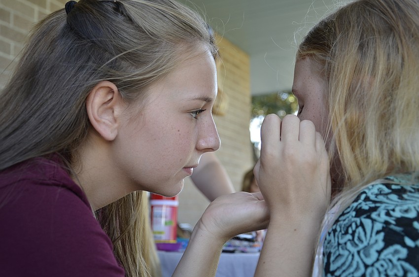Harley Kovalick, a Braden River High School volunteer, paints Abigail Tallent's face.