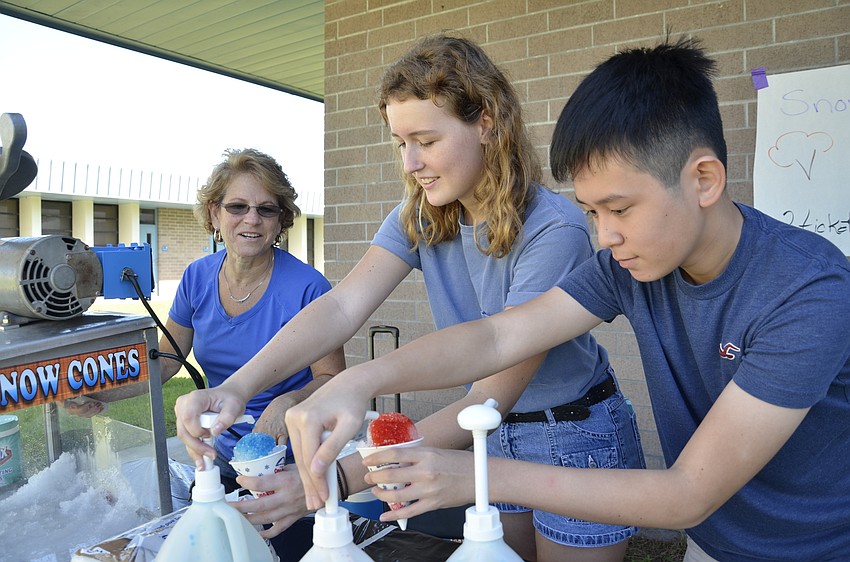 Fourth-grade teacher Mary Searing helps volunteers Elizabeth Gape and Vihn Dong make snow cones.