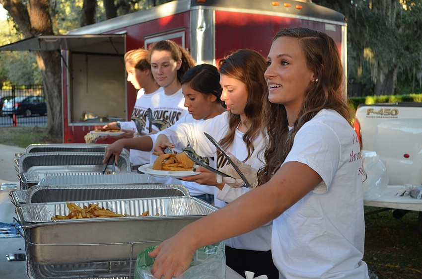 Jillian Santiago and members of the CMHS swim team help dish out fried fish and chicken for the occasion.
