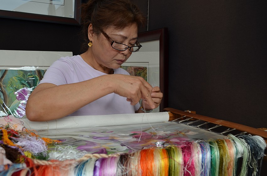 Artist Xiao Xia Zhang threads a needle through the fabric.