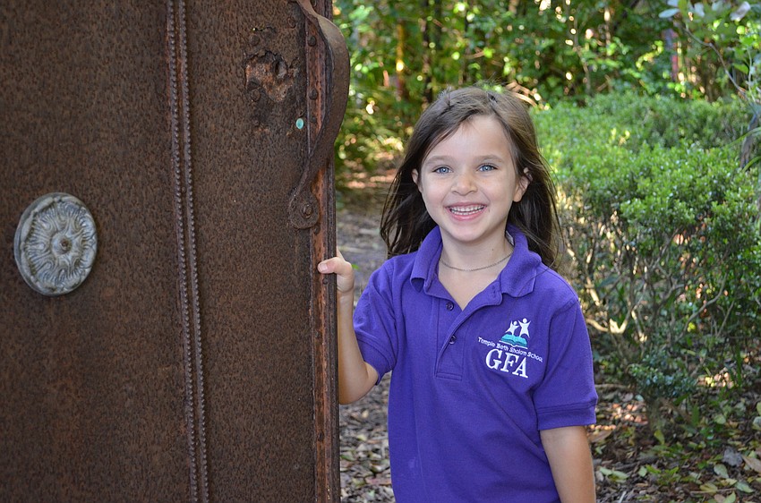 Adonia Brady holds open the door to the secret garden within the Sarasota Children's Garden.