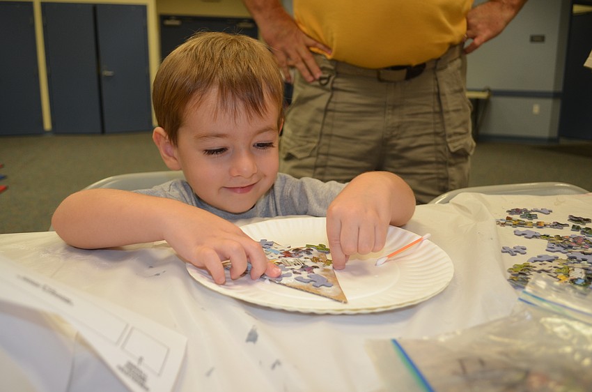 Three-year-old Hayden Keever, of Bradenton, uses glue and puzzle pieces to make his 3-D Christmas tree.
